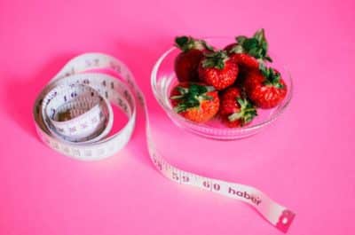 bowl of strawberries next to measuring tape on pink background for psychology of overeating symbols