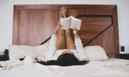 bored woman reading a book while lying on a bed
