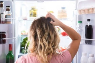 woman standing in front of the refrigerator scratching her head unsure of what to eat