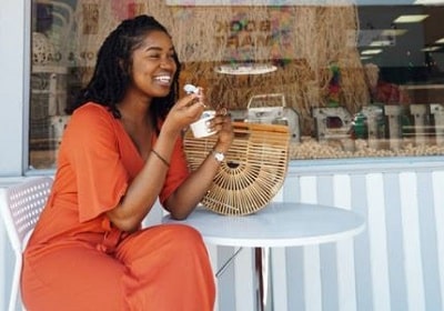 happy, smiling woman eating frozen yogurt at an outdoor table to show satisfied eating