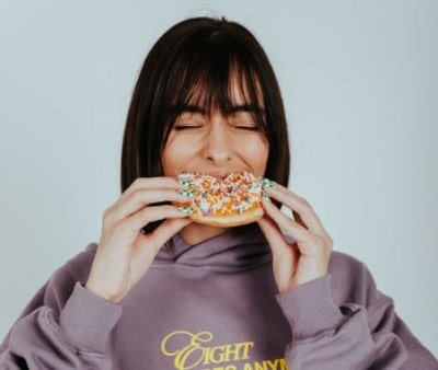 woman blissfully taking a bite of a donut without feeling guilty after eating
