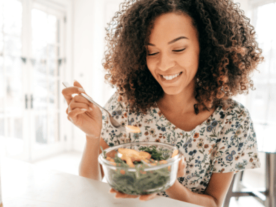 woman smiling and eating a healthy bowl of grains, veggies, and protein